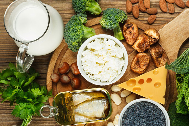 Natural Pharmaceuticals „CalciumControl™“ Pieno produktai, riešutai, žuvys ir daržovės ant medinio stalo, skirti sveikai mitybai ir baltymams.