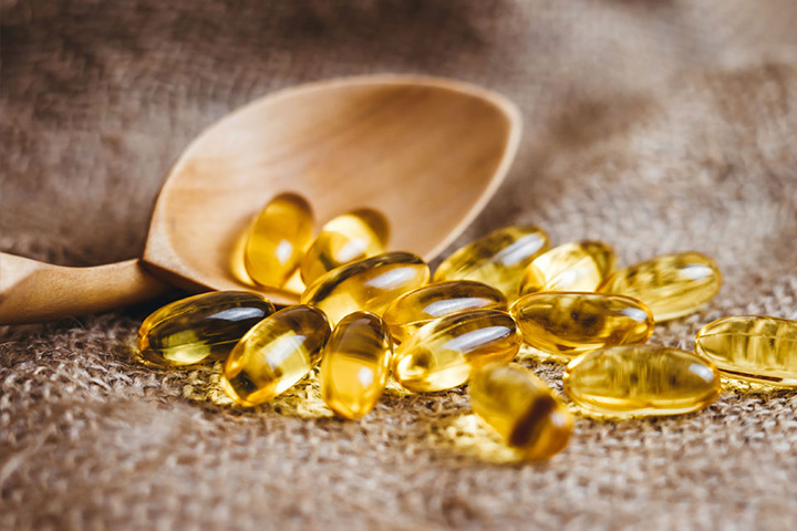 Natural Pharmaceuticals „CalciumControl™“ Geltoni skaidrūs omega-3 žuvų taukų kapsulės ant lino audinio šalia medinio šaukšto.