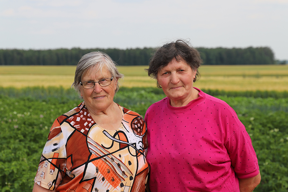 Natural Pharmaceuticals „CalciumControl™“ Dvi vyresnio amžiaus moterys stovi ūkyje prie žaliuojančių laukų ir žiūri į fotoaparatą.