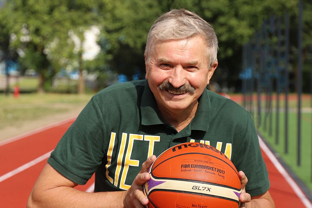 Natural Pharmaceuticals „CalciumControl™“ Laimingas vyresnis vyras lauke laiko krepšinio kamuolį prie sporto aikštelės.